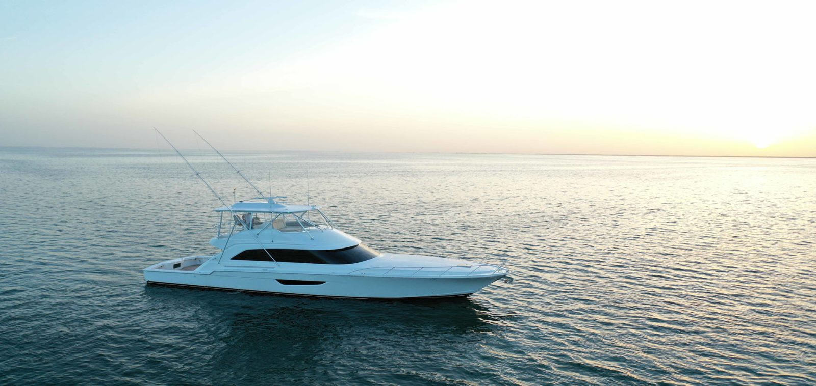 Betram Yachts 61 Convertible sportfisher cruising past a clear horizon at sunset on the open ocean.